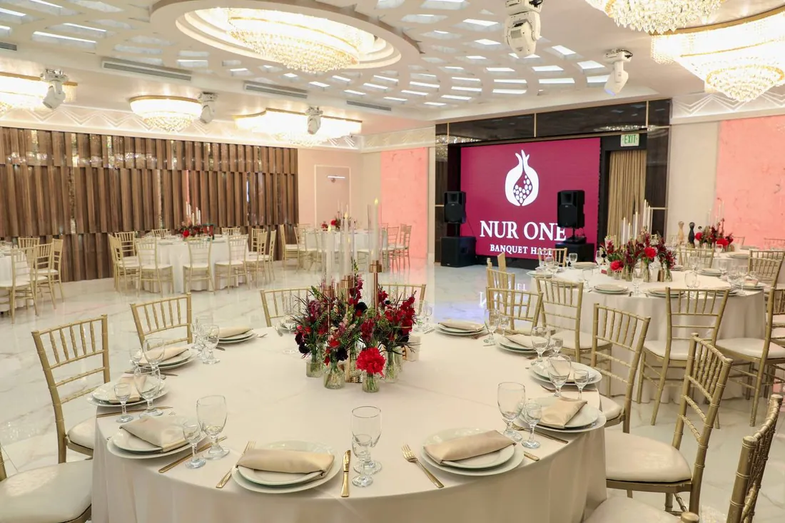 Wide view of the Nur One ballroom set for a reception, with the illuminated logo wall in the background